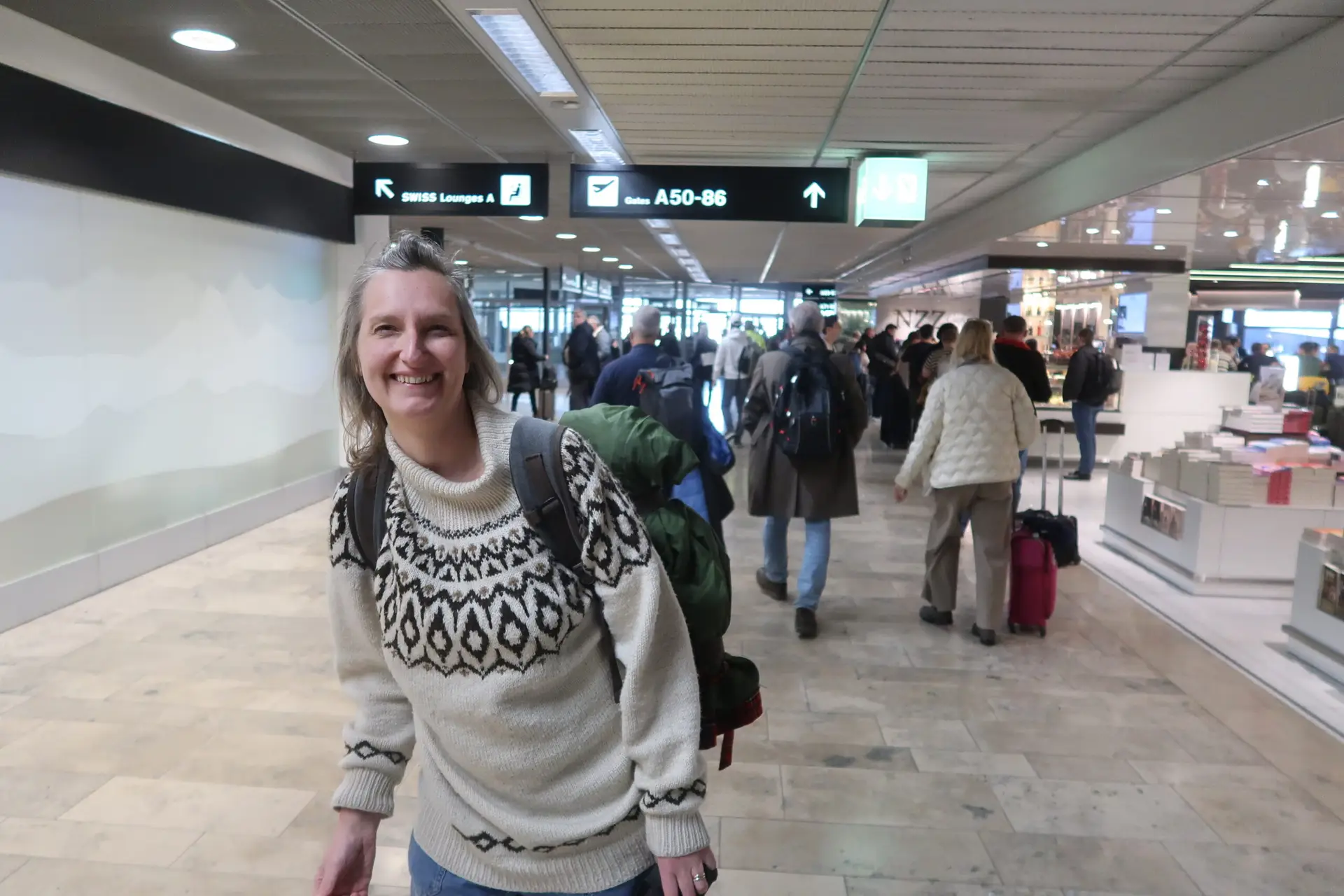 Psykologen står i en lufthavn med rygsæk, smilende og klar til rejse.